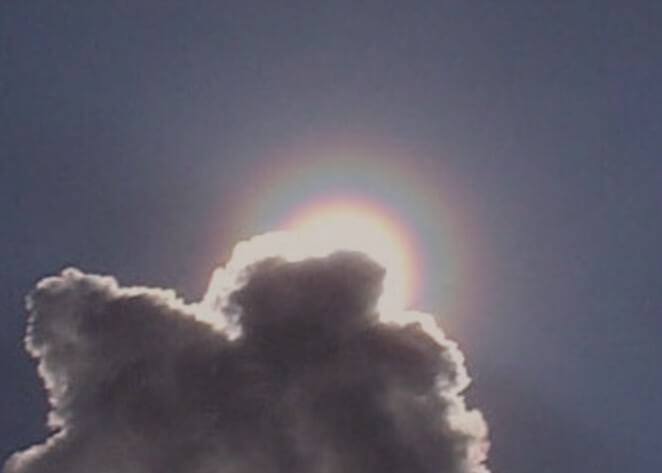 thick rainbow ring tight around the sun, partially obscured by a cloud.