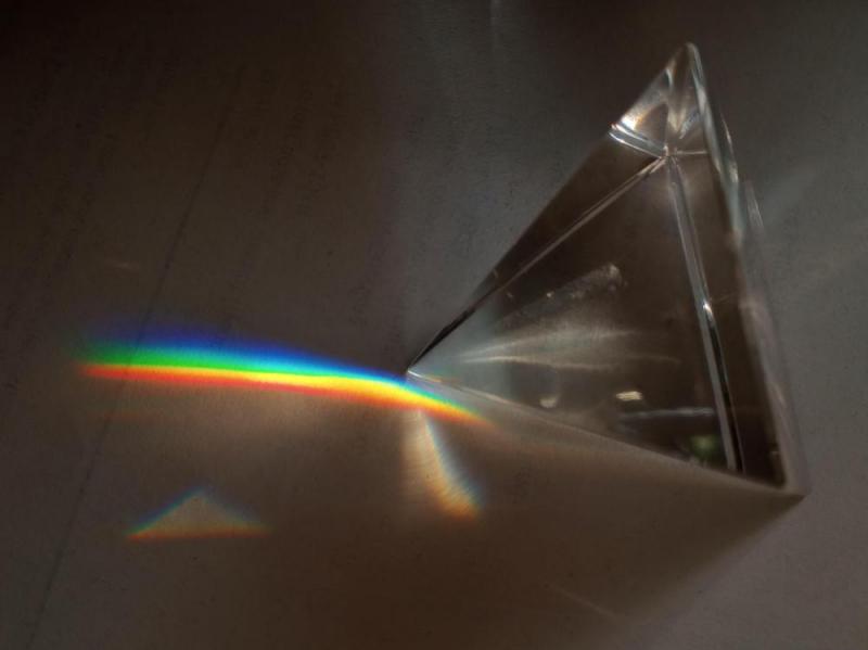 photo of a pyramid shaped crystal on one of its sides, casting a short rainbow on the counter